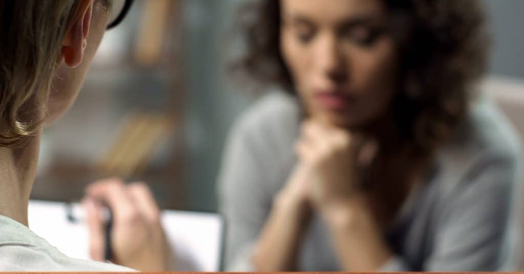 A female rehab patient looking in a mirror with her hands together while self-reflecting after a mental health therapy session at CRC's rehab center in Chicago.